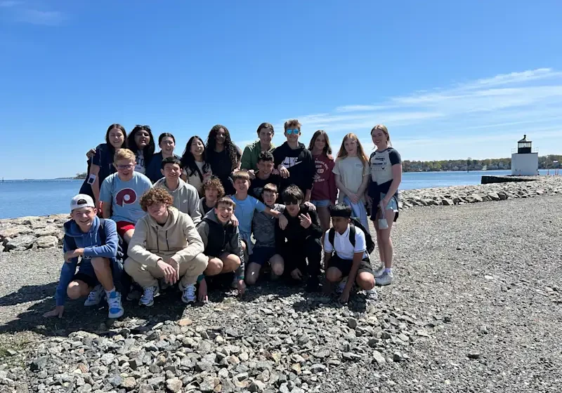 Teen group posing on rocky shore with lighthouse