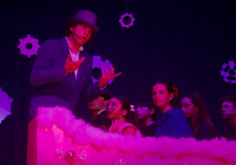 Top-hatted actor gestures amid pink stage fog